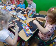Dzieci malują drewniane konie brązową i pomarańczową farbą.