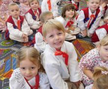 Dzieci w strojach ludowych siedzą na dywanie z uliczkami