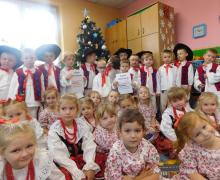 Dzieci z choinką w tle, chłopcy stoją a dziewczynki siedzą