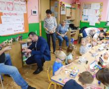 Dwóch mężczyzn struga koniki, dwie nauczycielki patrzą, a dzieci malują