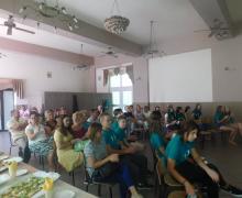 Grupa osób siedzących w sali na krzesłach zwróconych przodem