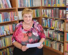 Kobieta w bibliotece, siedzi i trzyma w rękach kartkę